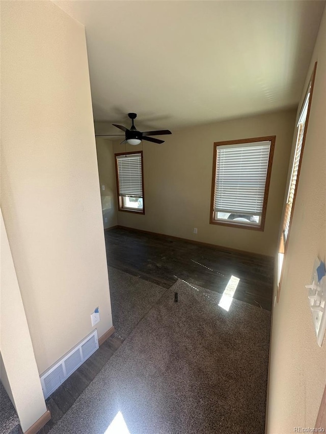 spare room with visible vents, dark carpet, baseboards, and a ceiling fan