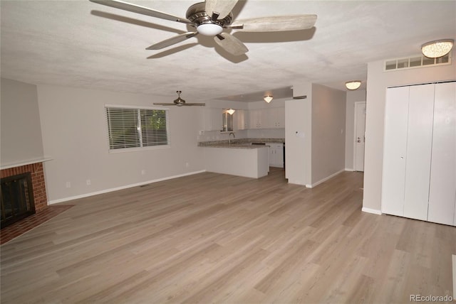 unfurnished living room with sink, a textured ceiling, a fireplace, and light hardwood / wood-style flooring