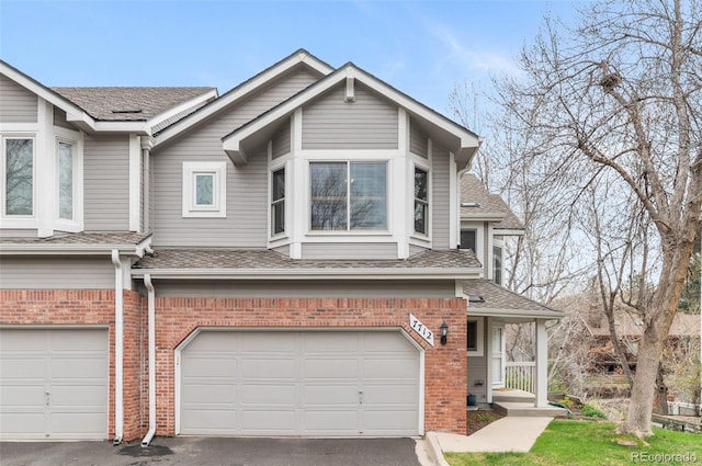 view of front of property with roof with shingles, an attached garage, driveway, and brick siding