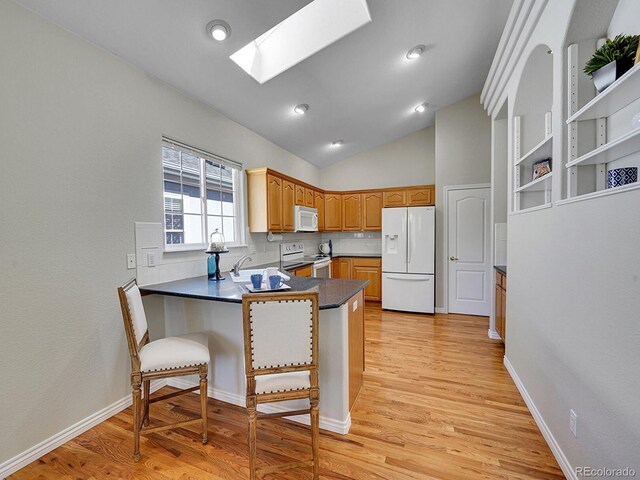 946 Champion Cir, Longmont, CO 80503 - kitchen with white appliances, a peninsula, a skylight, dark countertops, and light wood-style floors