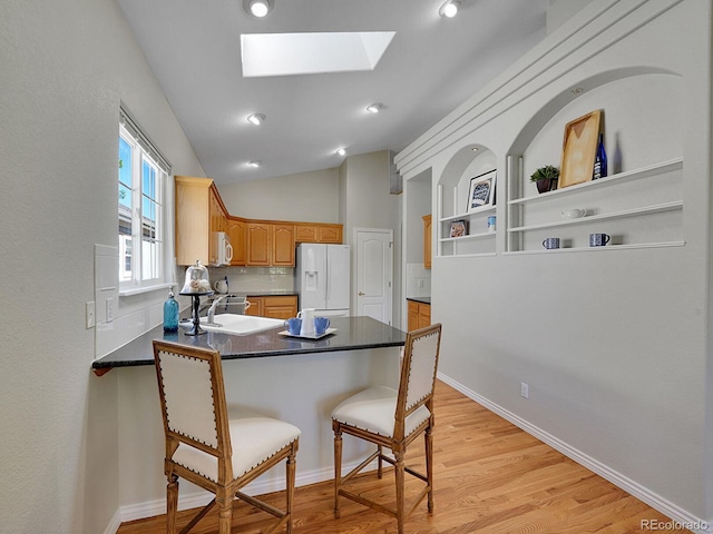 946 Champion Cir, Longmont, CO 80503 - kitchen with white appliances, a peninsula, a skylight, a kitchen breakfast bar, and dark countertops