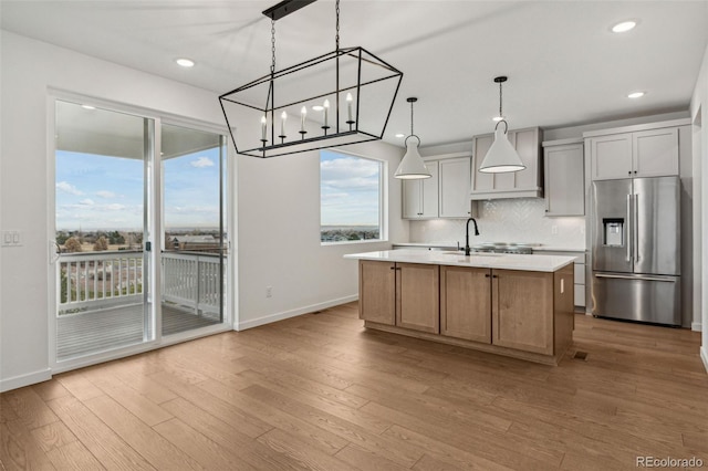 kitchen with pendant lighting, a kitchen island with sink, stainless steel refrigerator with ice dispenser, decorative backsplash, and light hardwood / wood-style floors