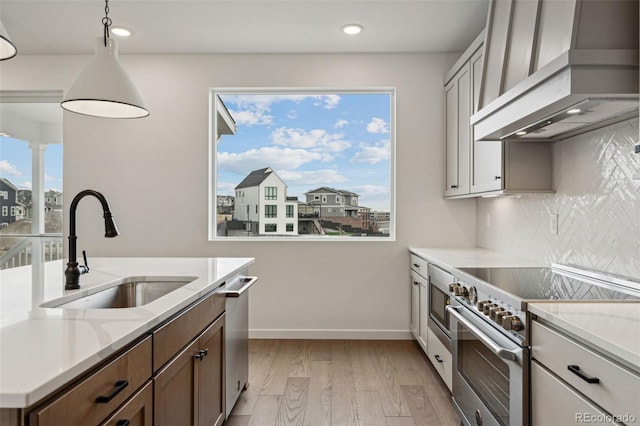 kitchen featuring appliances with stainless steel finishes, custom exhaust hood, sink, light hardwood / wood-style flooring, and hanging light fixtures