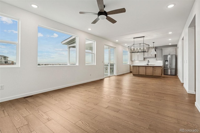 unfurnished living room with ceiling fan with notable chandelier, light hardwood / wood-style flooring, and sink