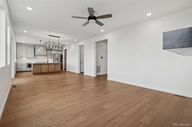 unfurnished living room with ceiling fan with notable chandelier and light wood-type flooring