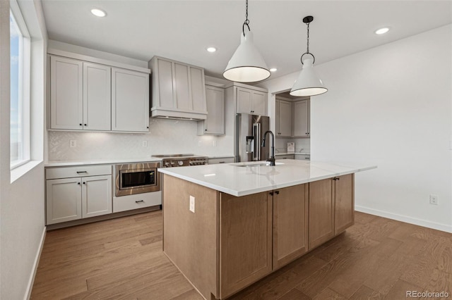 kitchen with pendant lighting, stainless steel appliances, light hardwood / wood-style floors, and an island with sink