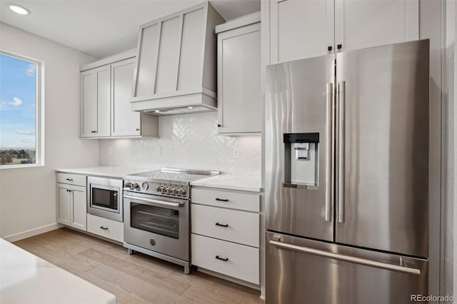 kitchen featuring white cabinets, light wood-type flooring, backsplash, and appliances with stainless steel finishes