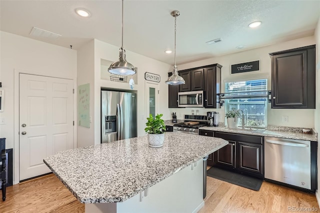 kitchen featuring sink, stainless steel appliances, light hardwood / wood-style floors, decorative light fixtures, and a kitchen island