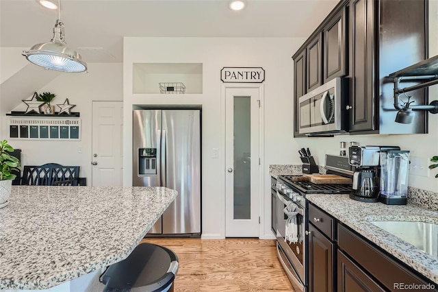 kitchen with dark brown cabinetry, stainless steel appliances, light stone counters, light hardwood / wood-style flooring, and a kitchen bar