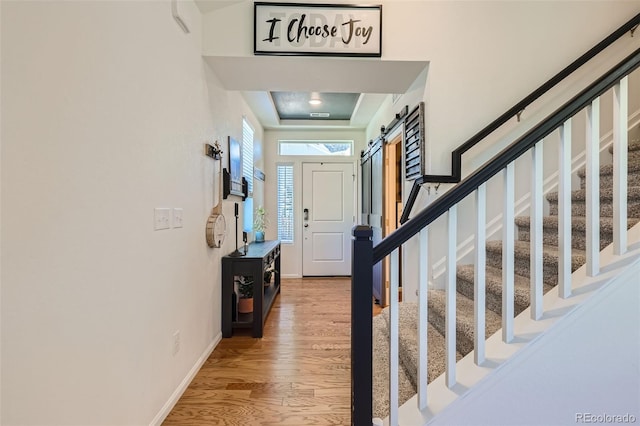 entryway with a tray ceiling, a barn door, and wood-type flooring