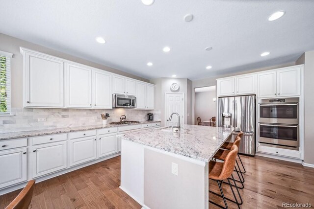 5865 Clover Ridge Cir, Castle Rock, CO 80104 - kitchen featuring appliances with stainless steel finishes, wood finished floors, decorative backsplash, white cabinets, and recessed lighting