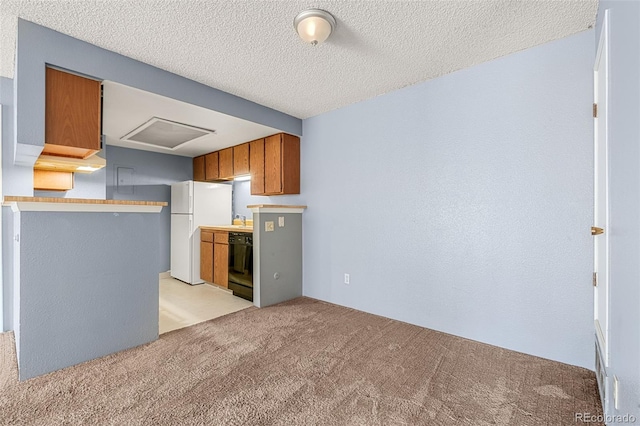 kitchen with a textured ceiling, light colored carpet, freestanding refrigerator, brown cabinets, and dishwasher