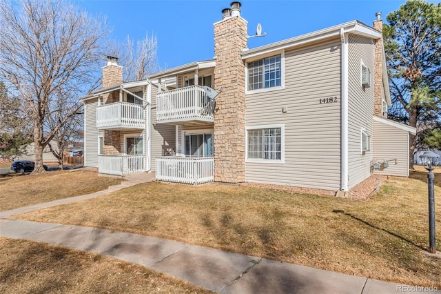 rear view of property with a balcony, a chimney, and a lawn