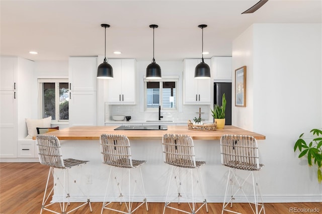 kitchen with wooden counters, stainless steel refrigerator, a kitchen breakfast bar, decorative backsplash, and white cabinets