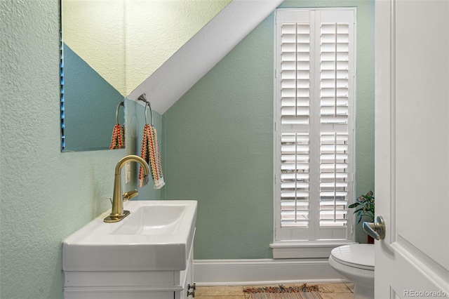 bathroom featuring vaulted ceiling, a textured wall, and toilet