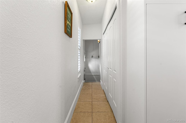 hall with a textured wall, baseboards, and light tile patterned floors