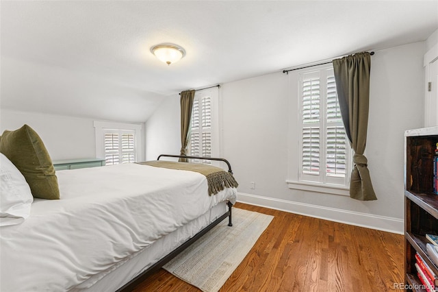 bedroom featuring multiple windows, vaulted ceiling, baseboards, and wood finished floors