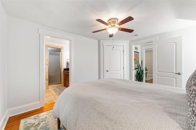 bedroom featuring light wood finished floors, baseboards, ensuite bath, ceiling fan, and a closet