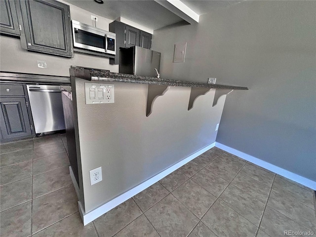 371 S Estes St Unit 10, Lakewood, CO 80226 - kitchen with stainless steel appliances, tile patterned floors, a breakfast bar, baseboards, and dark cabinets