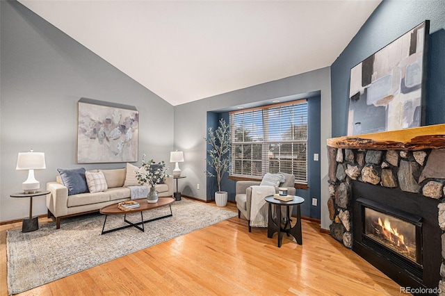 living room with wood finished floors, vaulted ceiling, a fireplace, and baseboards