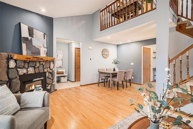 living room with stairs, a stone fireplace, wood finished floors, a high ceiling, and baseboards