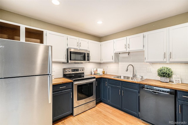kitchen featuring appliances with stainless steel finishes, butcher block counters, a sink, white cabinetry, and light wood-style flooring