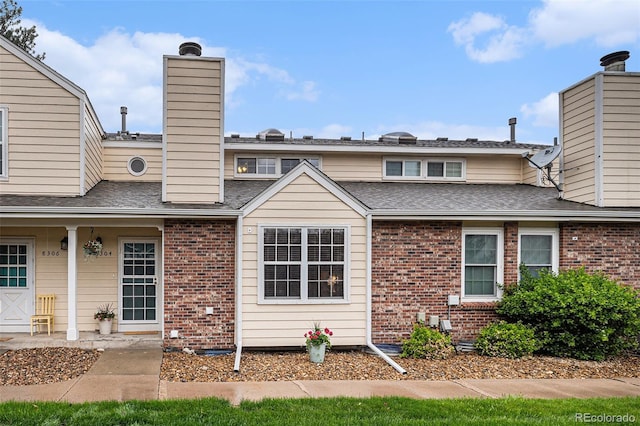 back of house featuring brick siding, a chimney, and a shingled roof