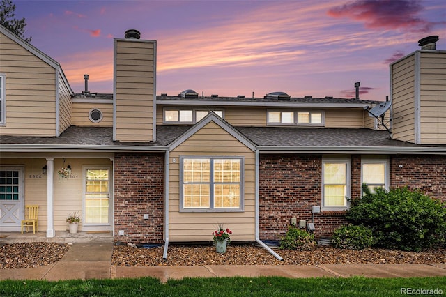 view of front of home featuring brick siding, a chimney, and a shingled roof