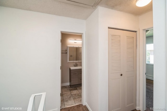 hallway featuring a textured ceiling, baseboard heating, sink, and tile patterned floors