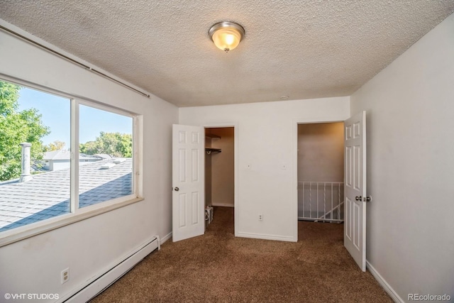 unfurnished bedroom featuring a walk in closet, a textured ceiling, baseboard heating, dark colored carpet, and a closet