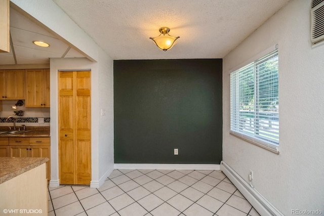 kitchen featuring sink, a baseboard heating unit, an AC wall unit, a textured ceiling, and light tile patterned flooring