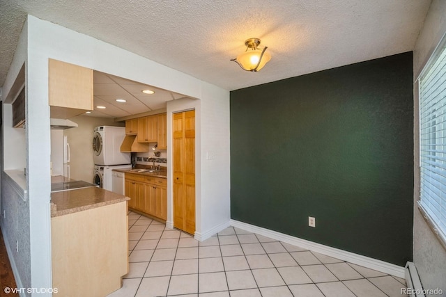 kitchen with sink, baseboard heating, stacked washer and dryer, a textured ceiling, and light tile patterned floors