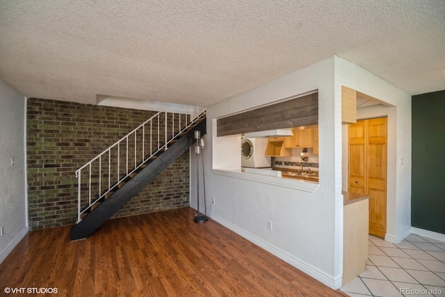 unfurnished living room with a textured ceiling, light wood-type flooring, stacked washer / dryer, and brick wall