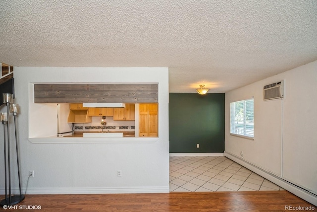 unfurnished living room with a wall unit AC, a baseboard radiator, a textured ceiling, and light wood-type flooring