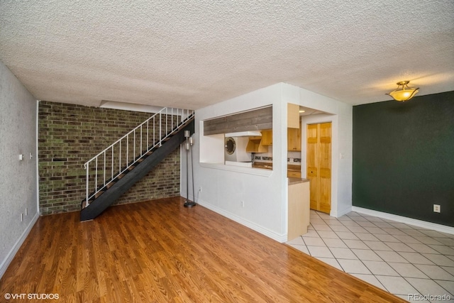 unfurnished living room with a textured ceiling, light hardwood / wood-style floors, washer / clothes dryer, and brick wall