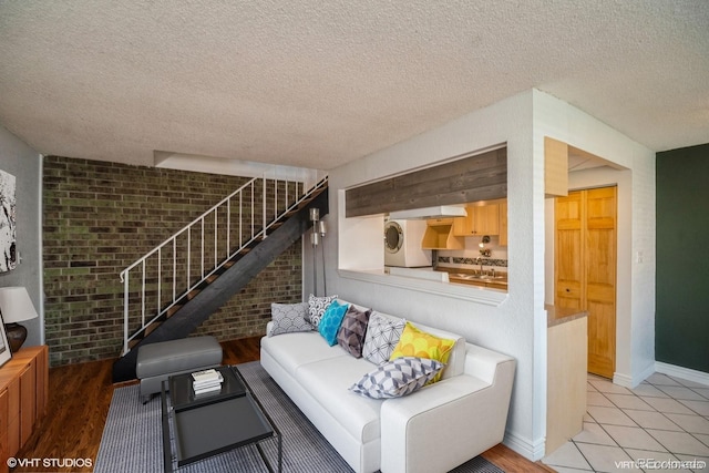 living room with a textured ceiling, light hardwood / wood-style floors, brick wall, and washer / dryer