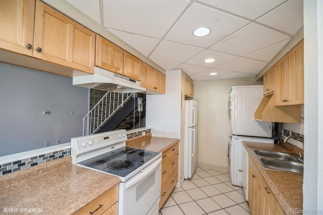 kitchen featuring sink, a drop ceiling, stacked washer / dryer, white appliances, and light tile patterned floors