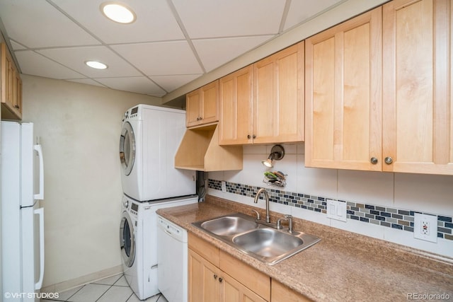 kitchen with light brown cabinetry, white appliances, stacked washer / dryer, and sink