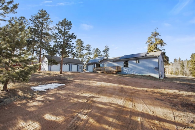 ranch-style house with dirt driveway, a detached garage, a deck, and roof mounted solar panels