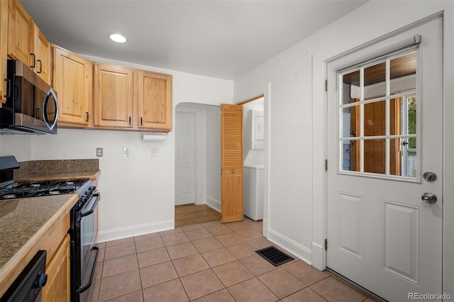 502 E San Miguel St, Colorado Springs, CO 80903 - kitchen with black range with gas cooktop, stainless steel microwave, stacked washing machine and dryer, light tile patterned floors, and light brown cabinets