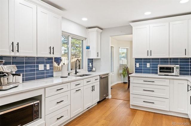 kitchen featuring backsplash, sink, light hardwood / wood-style flooring, dishwasher, and white cabinetry