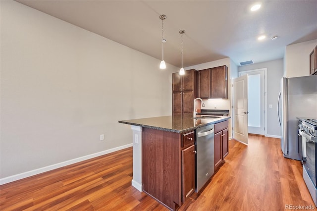 kitchen featuring appliances with stainless steel finishes, sink, a center island with sink, decorative light fixtures, and hardwood / wood-style floors