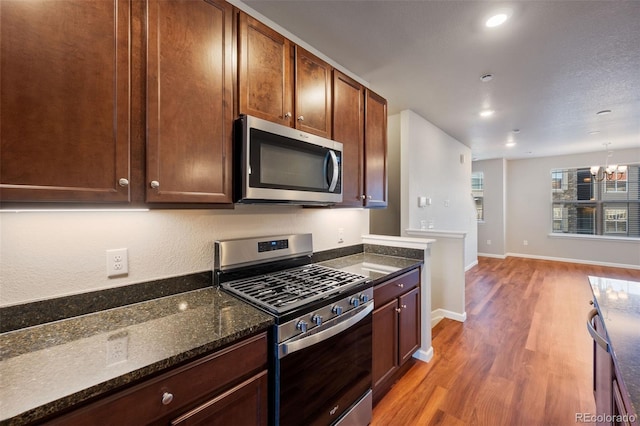 kitchen with dark hardwood / wood-style flooring, a notable chandelier, dark stone countertops, pendant lighting, and appliances with stainless steel finishes