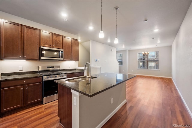 kitchen featuring sink, dark wood-type flooring, stainless steel appliances, and an island with sink