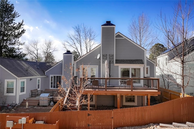 back of property featuring a deck, a chimney, and a fenced front yard