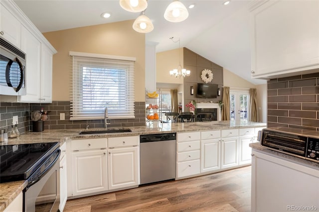 kitchen featuring hanging light fixtures, vaulted ceiling, stainless steel appliances, white cabinetry, and a sink