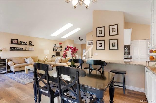 dining space with vaulted ceiling with skylight, wine cooler, light wood-style flooring, a notable chandelier, and stairway