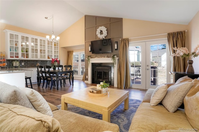 living room with french doors, a notable chandelier, dark wood-type flooring, high vaulted ceiling, and a tile fireplace