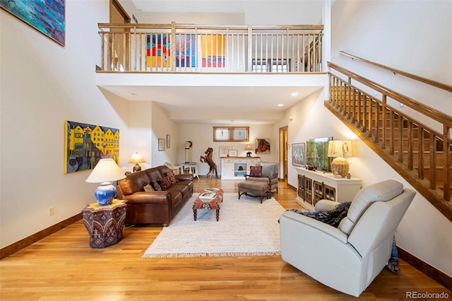 living area with baseboards, stairs, wood finished floors, and a towering ceiling