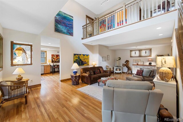living area with a healthy amount of sunlight, baseboards, light wood finished floors, and a towering ceiling